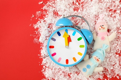 Alarm clock and snowmen in pile of snow on red background, flat lay with space for text. New Year countdown