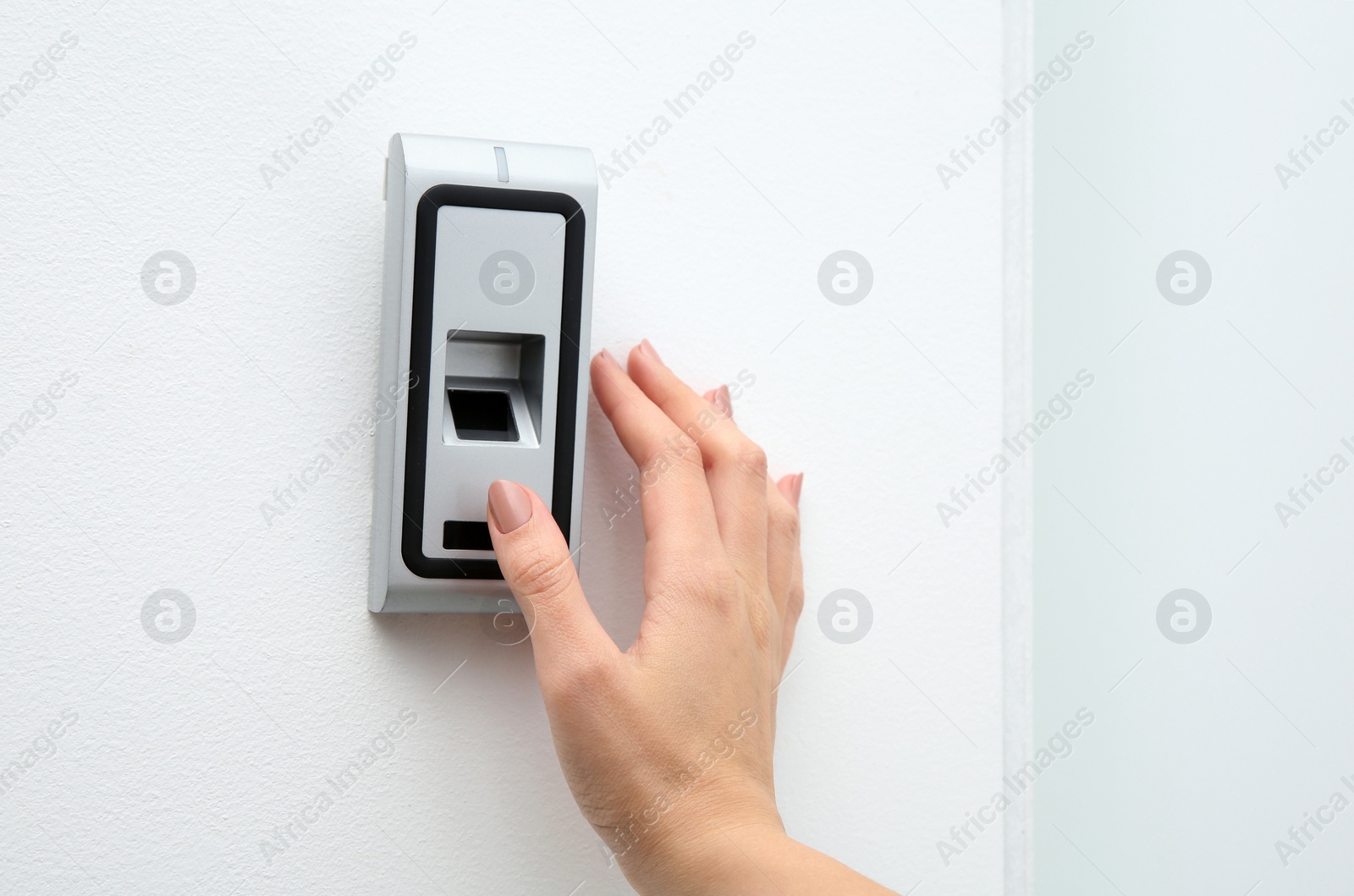 Photo of Young woman pressing fingerprint scanner on alarm system indoors