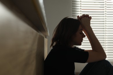 Sad young woman sitting indoors, space for text