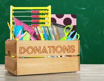 Image of Donation box with different school stationery on white wooden table near chalkboard