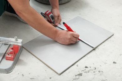 Photo of Worker measuring and marking ceramic tile on floor, closeup