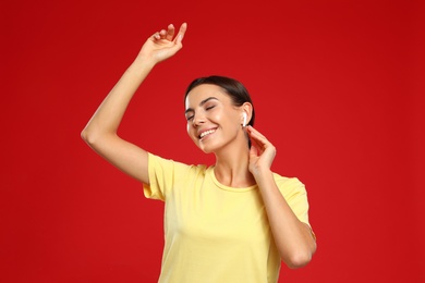 Photo of Happy young woman listening to music through wireless earphones on red background