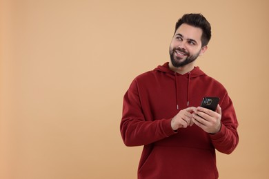 Happy young man using smartphone on beige background, space for text