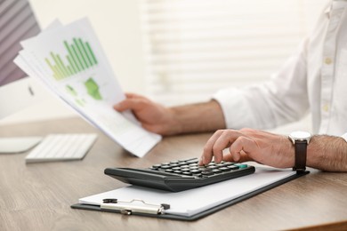 Photo of Professional accountant using calculator at wooden desk in office, closeup