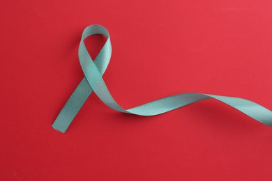 Photo of Turquoise awareness ribbon on red background, top view