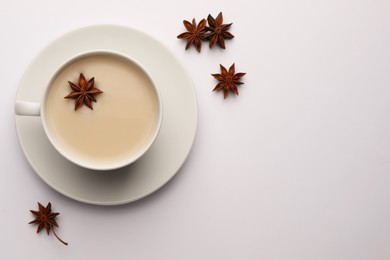 Cup of tea with milk and anise stars on white table, flat lay. Space for text