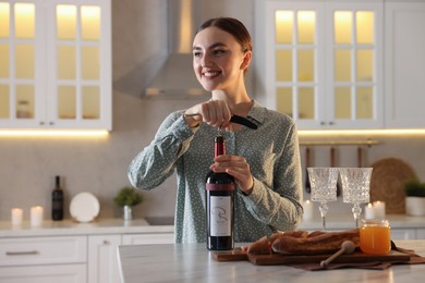 Photo of Romantic dinner. Woman opening wine bottle with corkscrew at table in kitchen