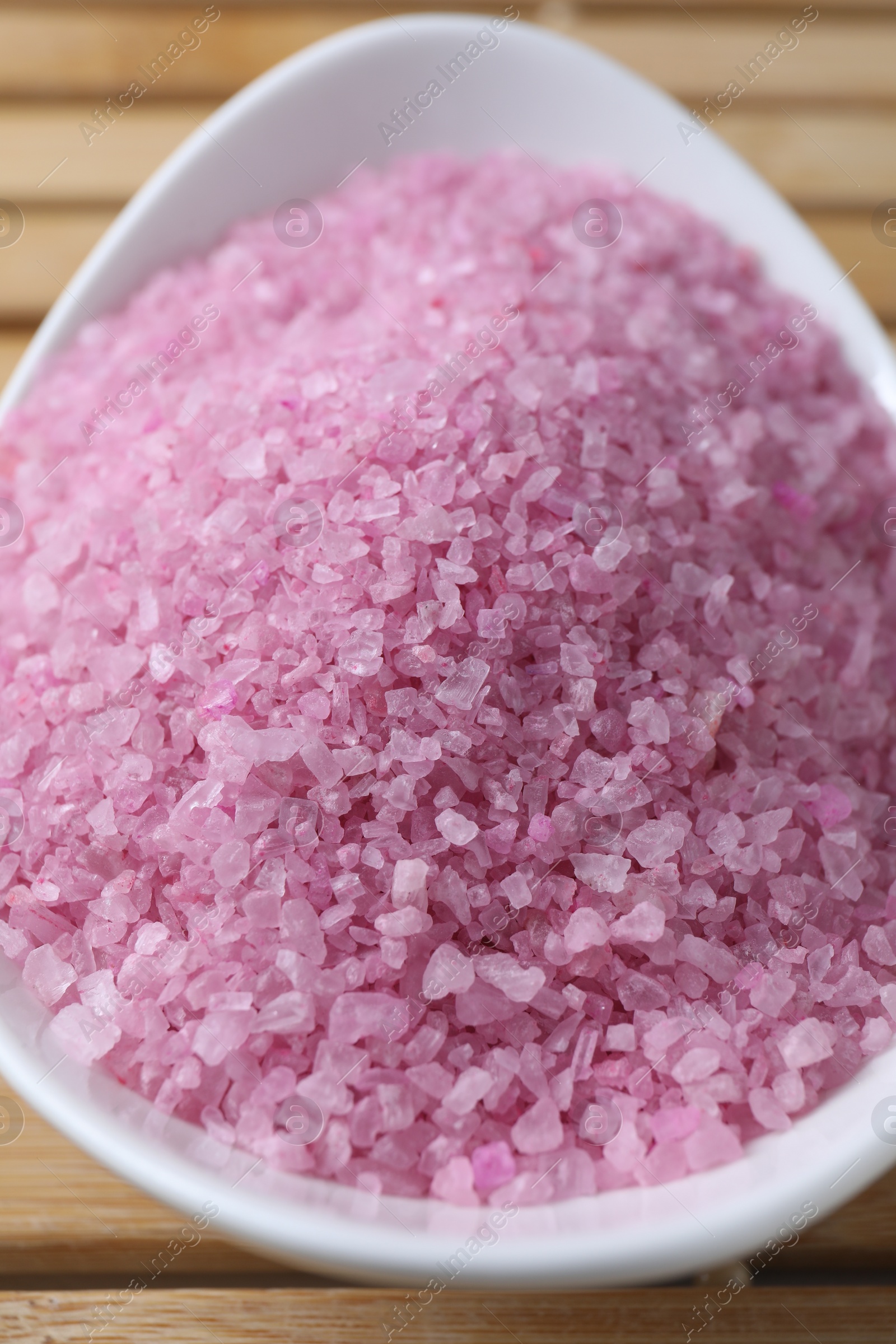 Photo of Bowl with pink sea salt on wooden table, closeup