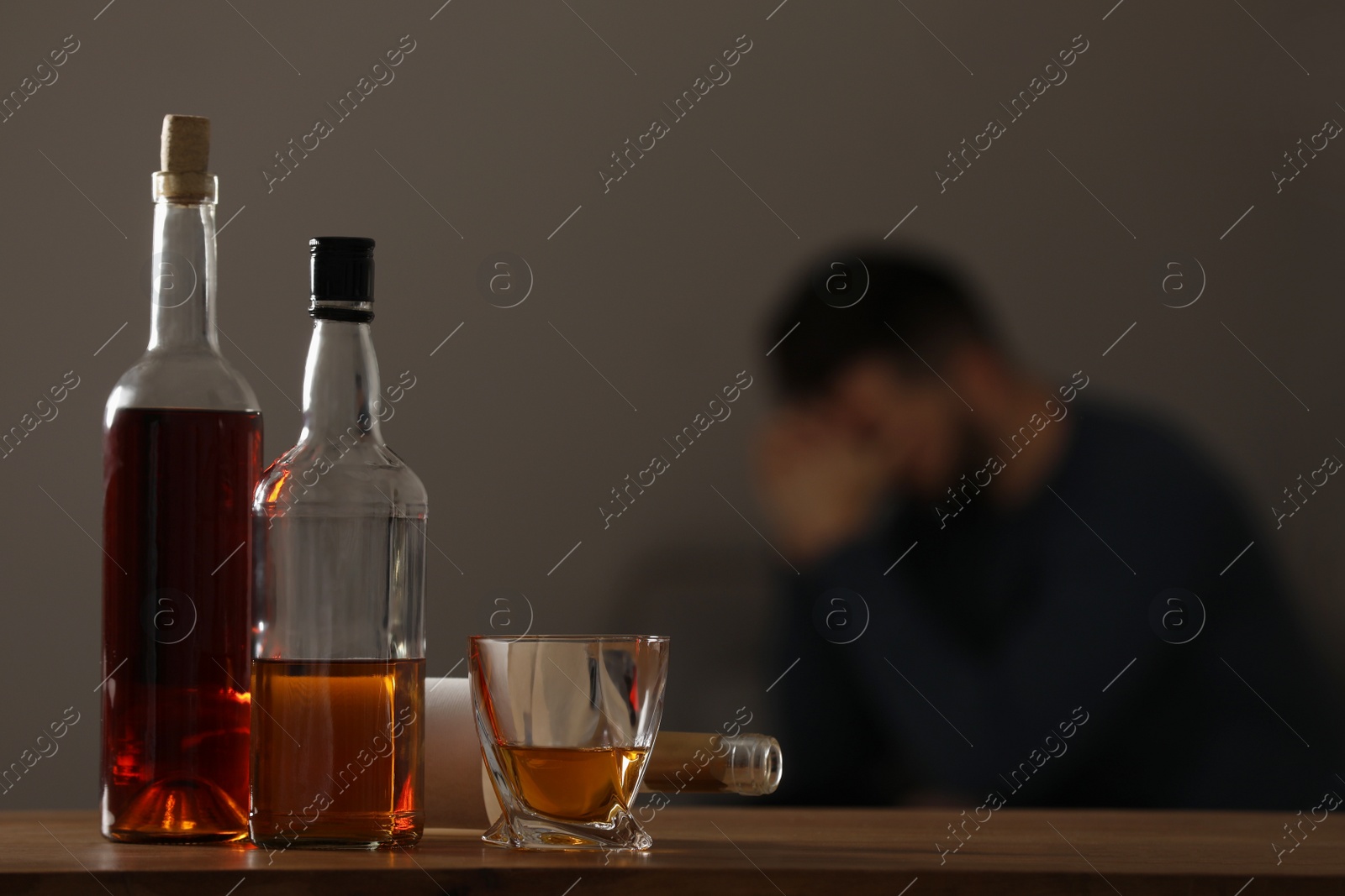 Photo of Addicted man at home, focus on table with alcoholic drinks. Space for text