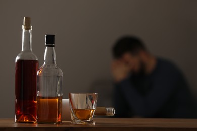 Photo of Addicted man at home, focus on table with alcoholic drinks. Space for text