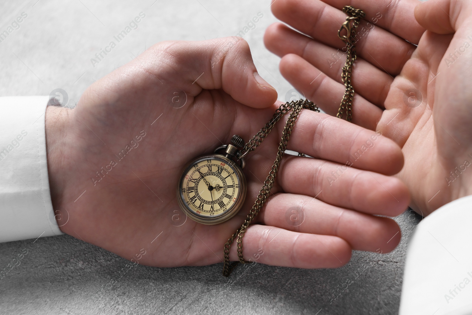 Photo of Man holding chain with elegant pocket watch at grey textured table, closeup