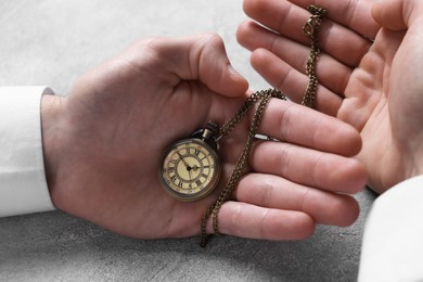 Man holding chain with elegant pocket watch at grey textured table, closeup