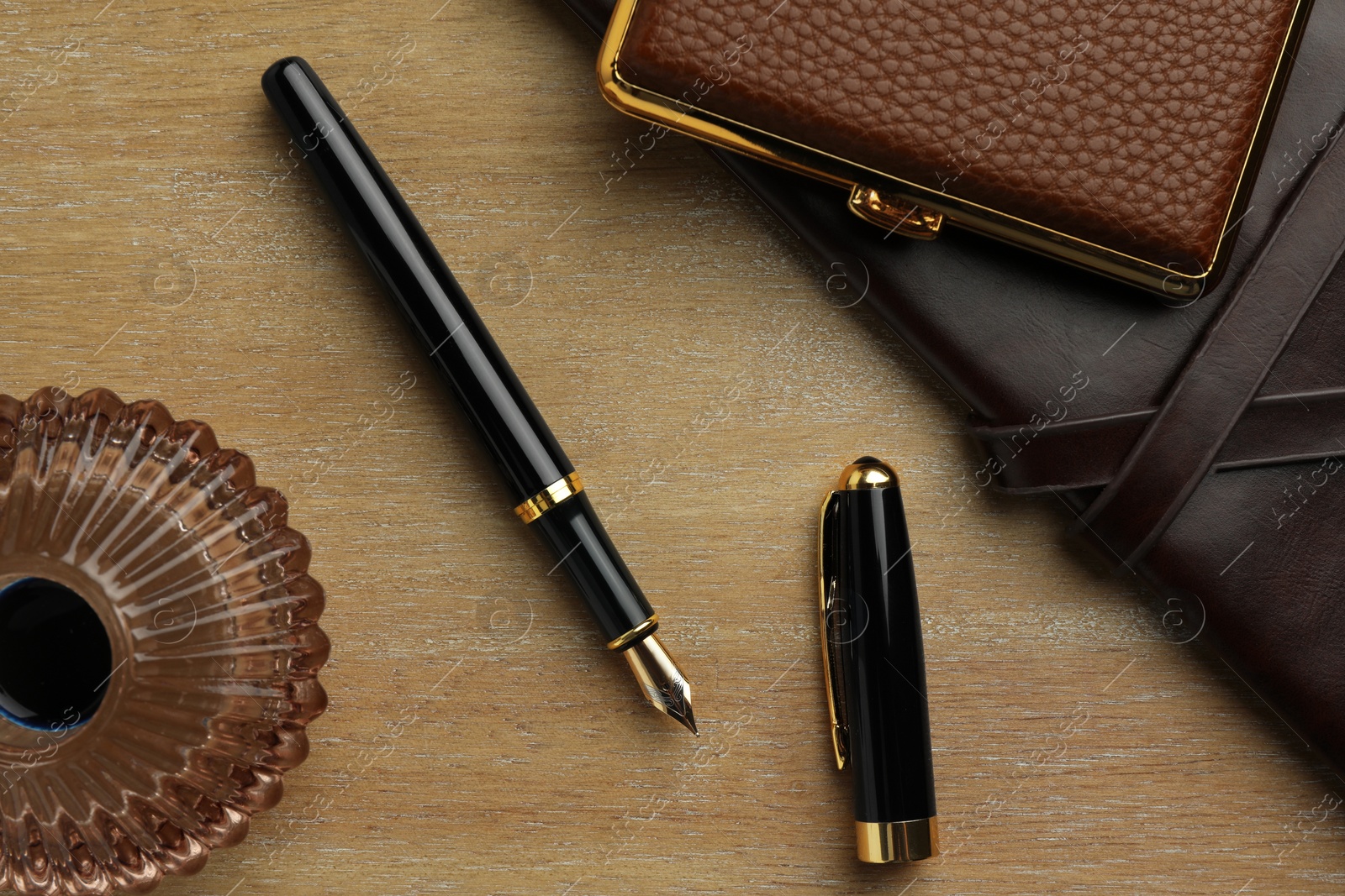 Photo of Stylish fountain pen, notebook, inkwell and cigarette case on wooden table, flat lay