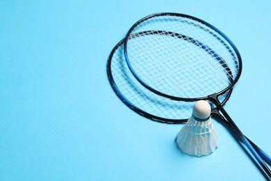 Photo of Feather badminton shuttlecocks and rackets on light blue background, space for text