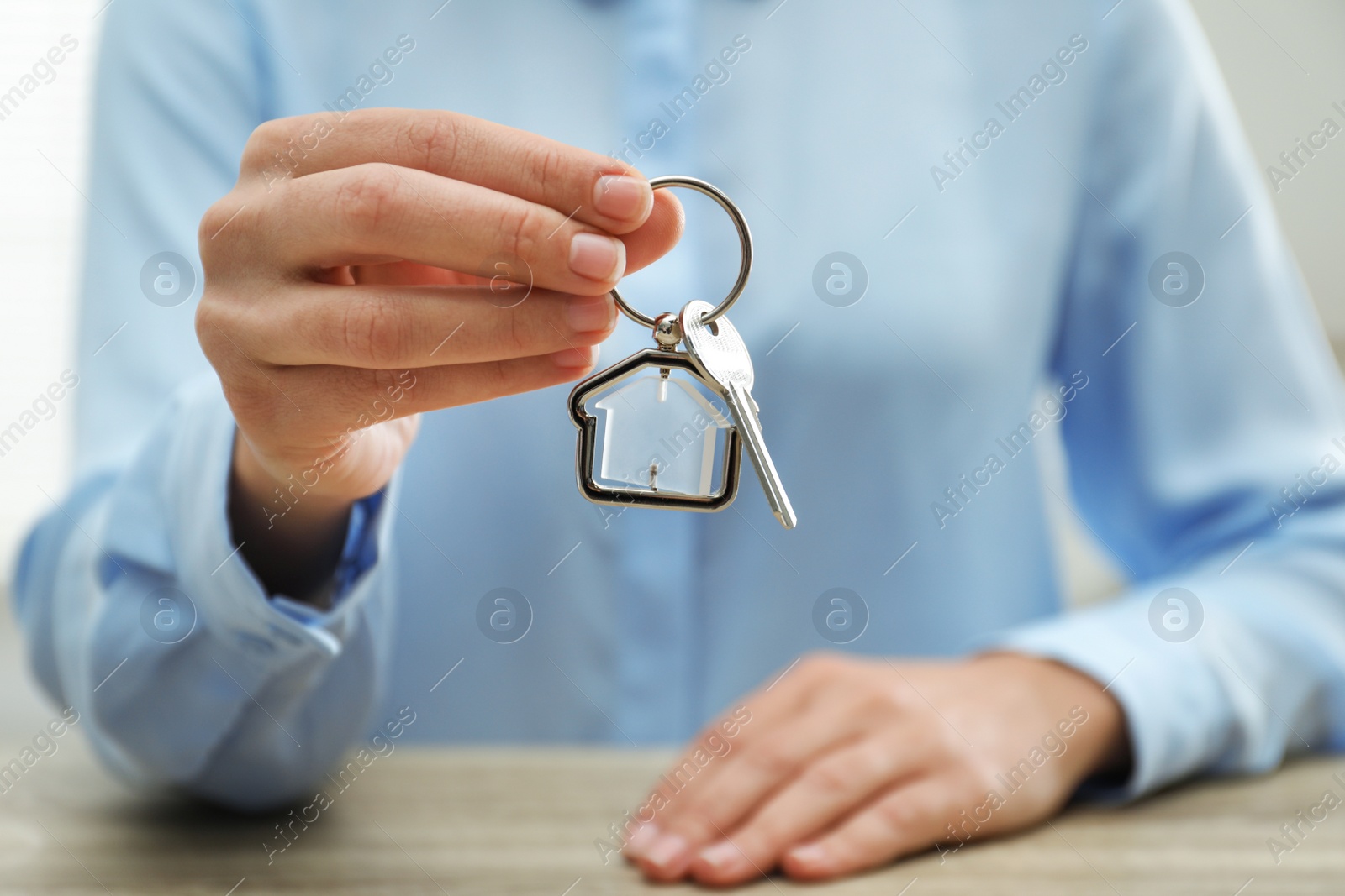 Photo of Real estate agent holding house key with trinket at wooden table, closeup