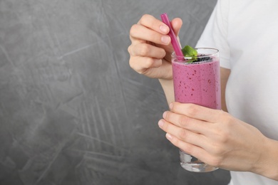 Young woman holding glass of tasty blackberry smoothie on grey background, closeup. Space for text