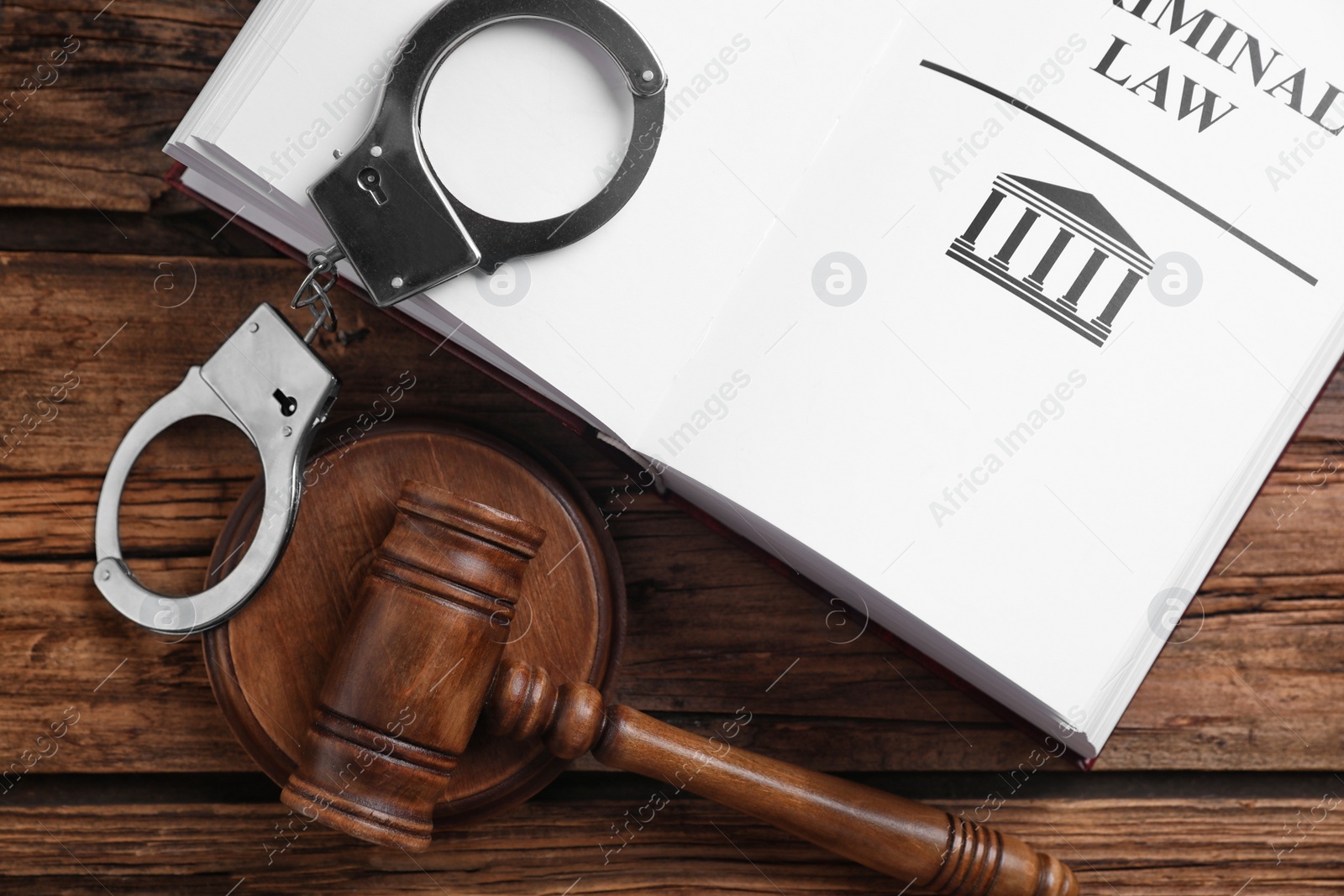 Photo of Book with words CRIMINAL LAW, handcuffs and gavel on wooden table, flat lay