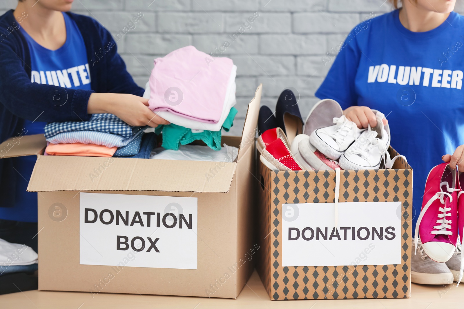 Photo of Female volunteers collecting clothes and shoes into donation boxes indoors