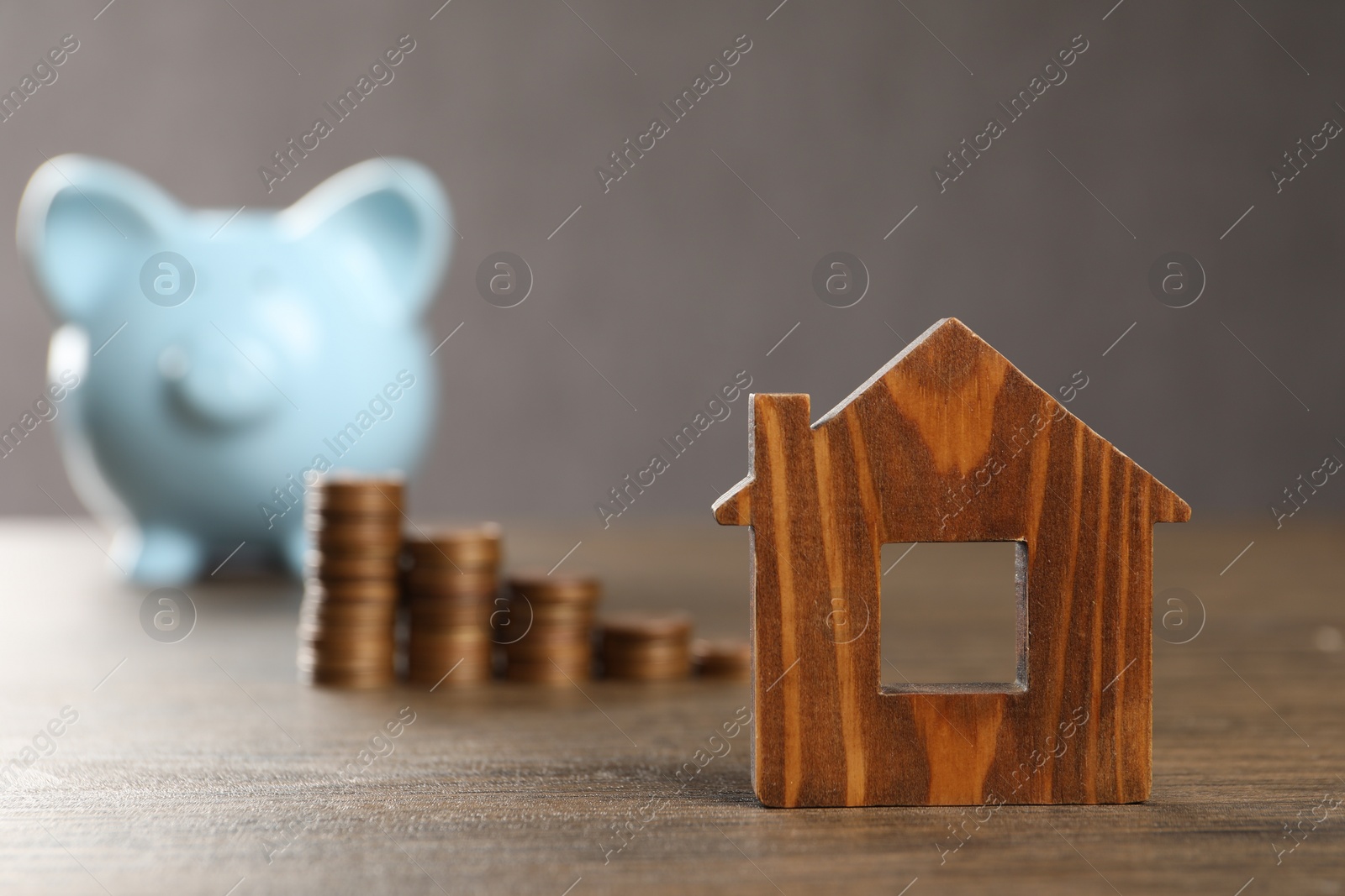 Photo of House model, piggy bank and stacked coins on wooden table, selective focus