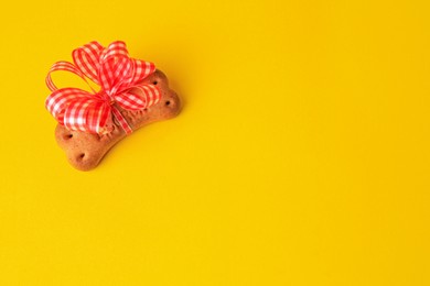 Photo of Bone shaped dog cookie with bow on yellow background, above view. Space for text