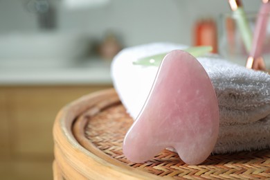 Photo of Rose quartz gua sha tool and soft towel on wicker table indoors, closeup. Space for text