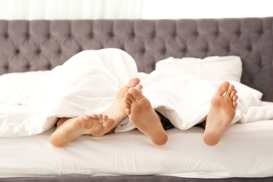 Gay couple cuddling under blanket on bed, closeup of feet