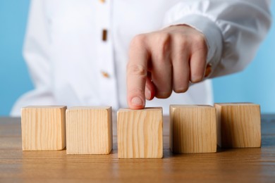 Photo of Woman arranging empty cubes in row on wooden table, closeup. Space for text