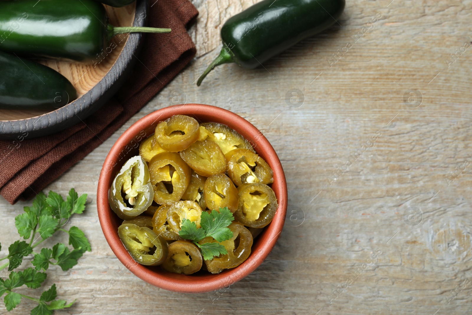 Photo of Fresh and pickled green jalapeno peppers on wooden table, flat lay. Space for text