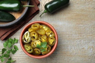 Photo of Fresh and pickled green jalapeno peppers on wooden table, flat lay. Space for text