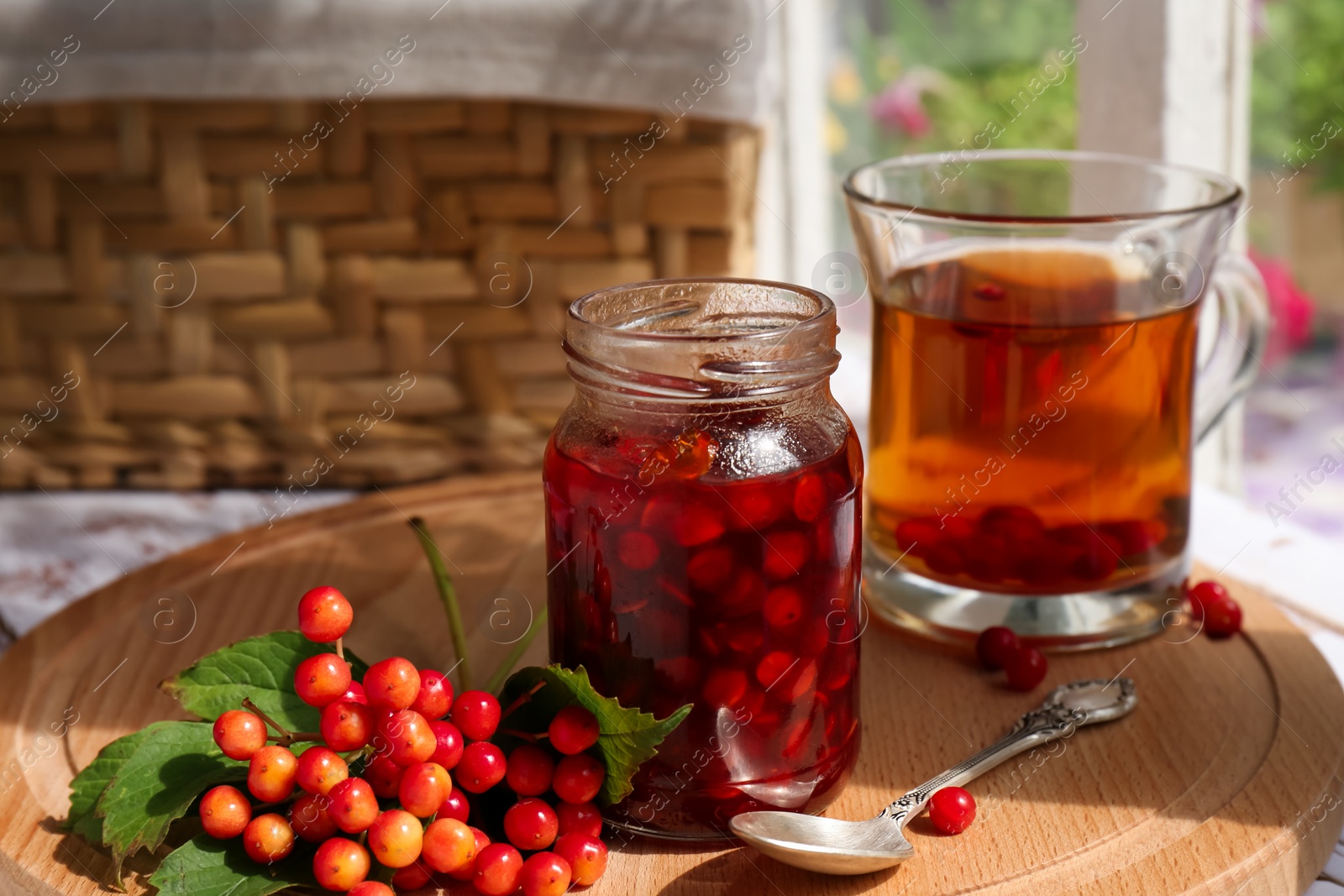 Photo of Tasty hot drink, jam and viburnum berries on wooden board indoors