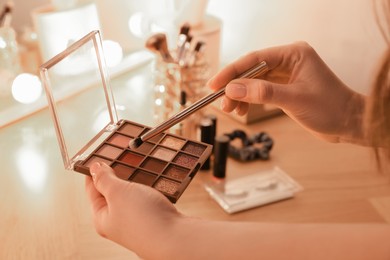 Photo of Woman with eyeshadow palette and brush at dressing table, closeup