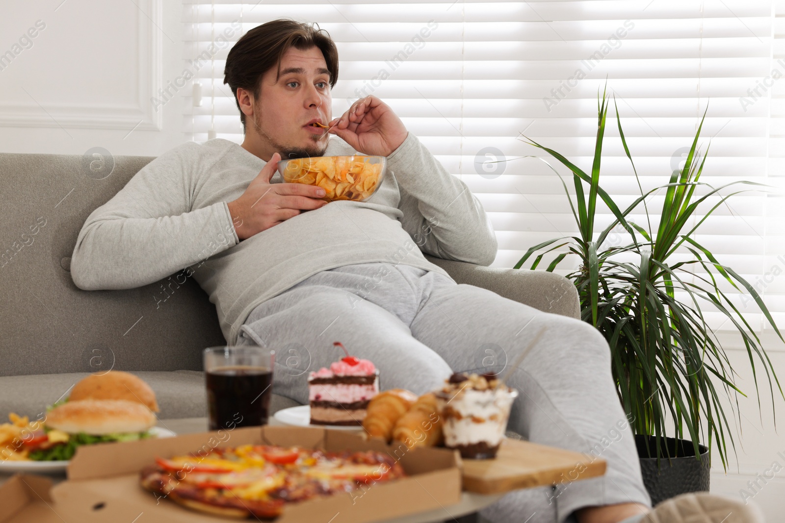 Photo of Overweight man with chips on sofa at home