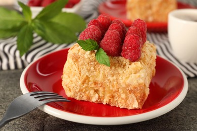 Photo of Piece of delicious Napoleon cake with fresh raspberries served on grey table, closeup