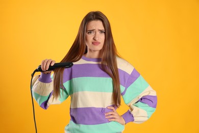 Photo of Upset young woman with flattening iron on yellow background. Hair damage