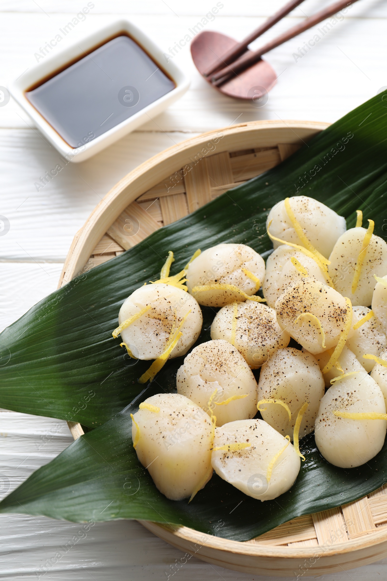 Photo of Raw scallops with milled pepper, lemon zest and soy sauce on white wooden table, flat lay