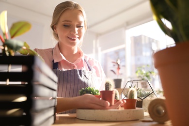 Photo of Young beautiful woman taking care of home plants at table indoors, space for text