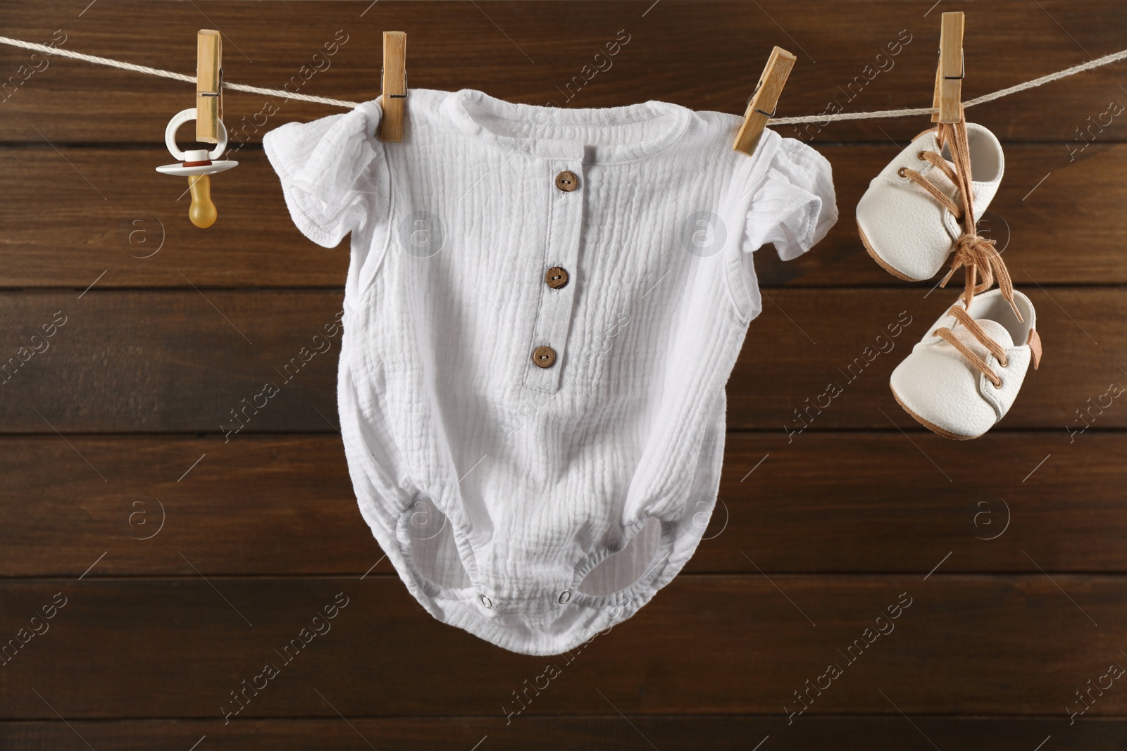 Photo of Baby clothes and accessories hanging on washing line near wooden wall