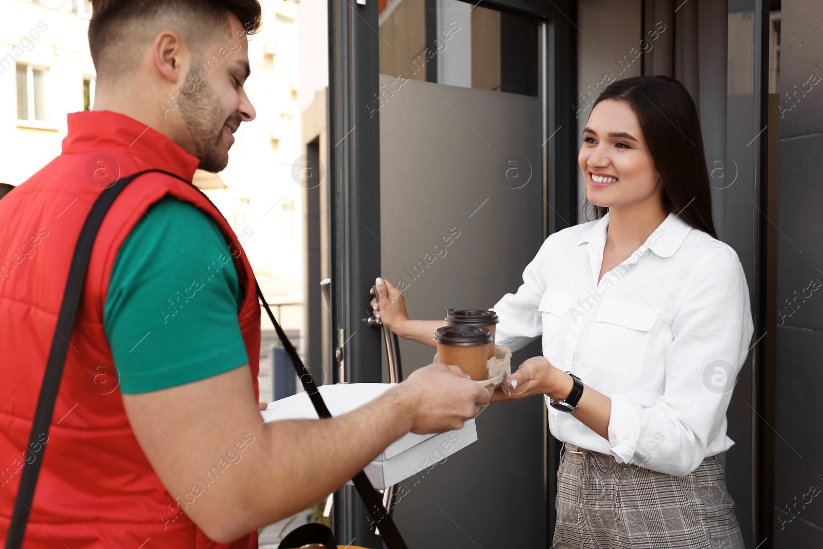 Photo of Courier giving order to young woman at open door. Food delivery service