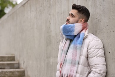 Photo of Handsome man in warm scarf near wall outdoors. Space for text