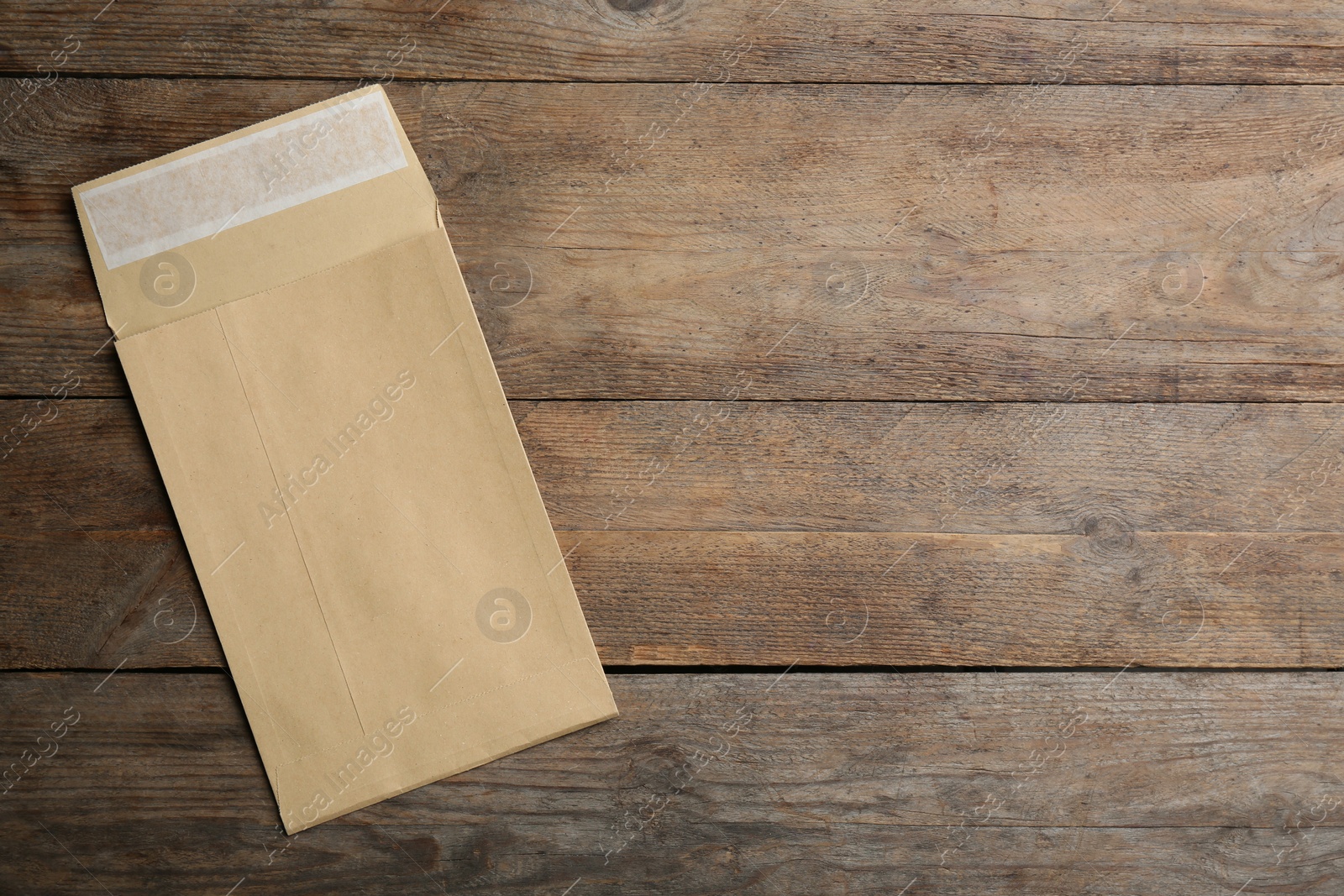 Photo of Kraft paper envelope on wooden background, top view. Space for text