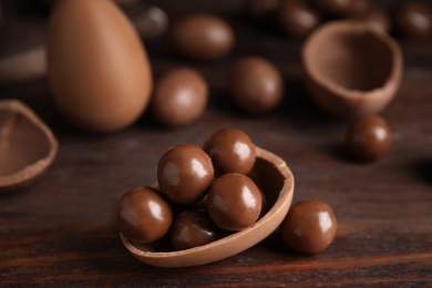 Photo of Half of tasty chocolate egg with candies on wooden table, closeup. Space for text