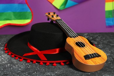 Black Flamenco hat and ukulele on dark textured table, closeup