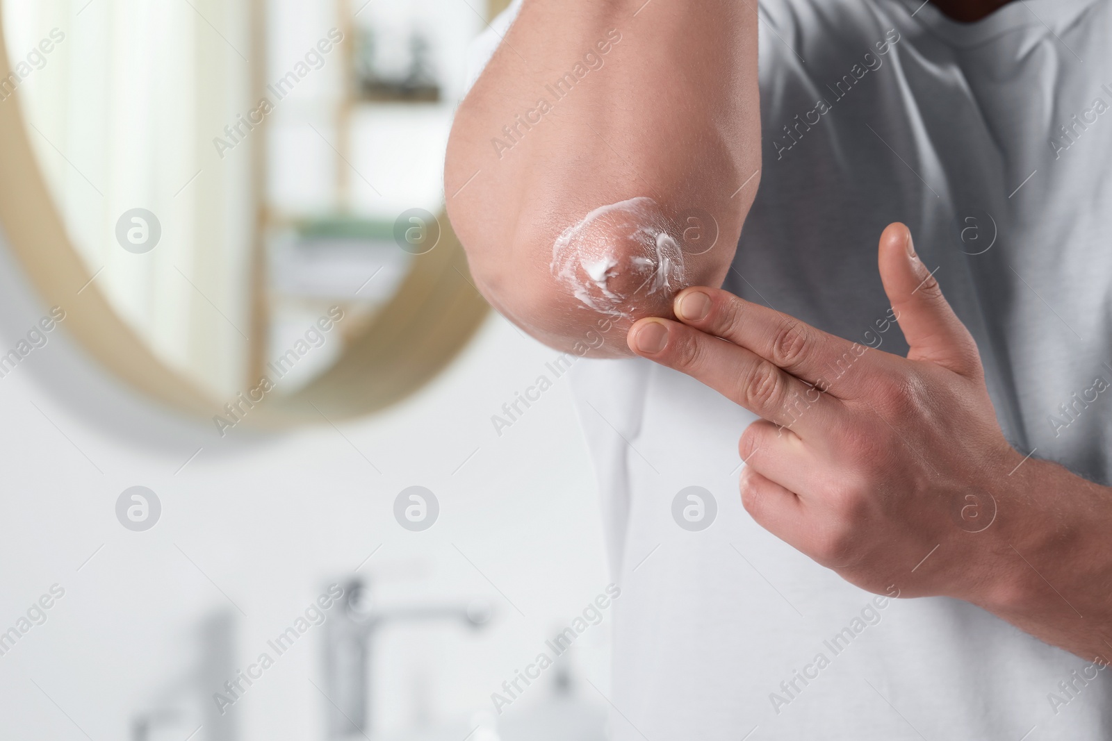 Photo of Man applying body cream onto his elbow in bathroom, closeup. Space for text