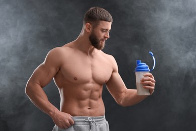 Photo of Young man with muscular body holding shaker of protein on dark grey background