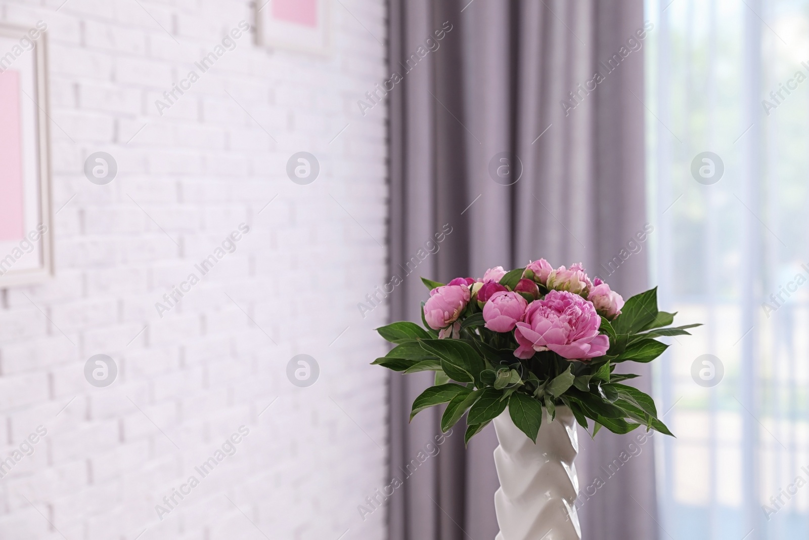 Photo of Vase with bouquet of beautiful peonies at white wall in room, space for text