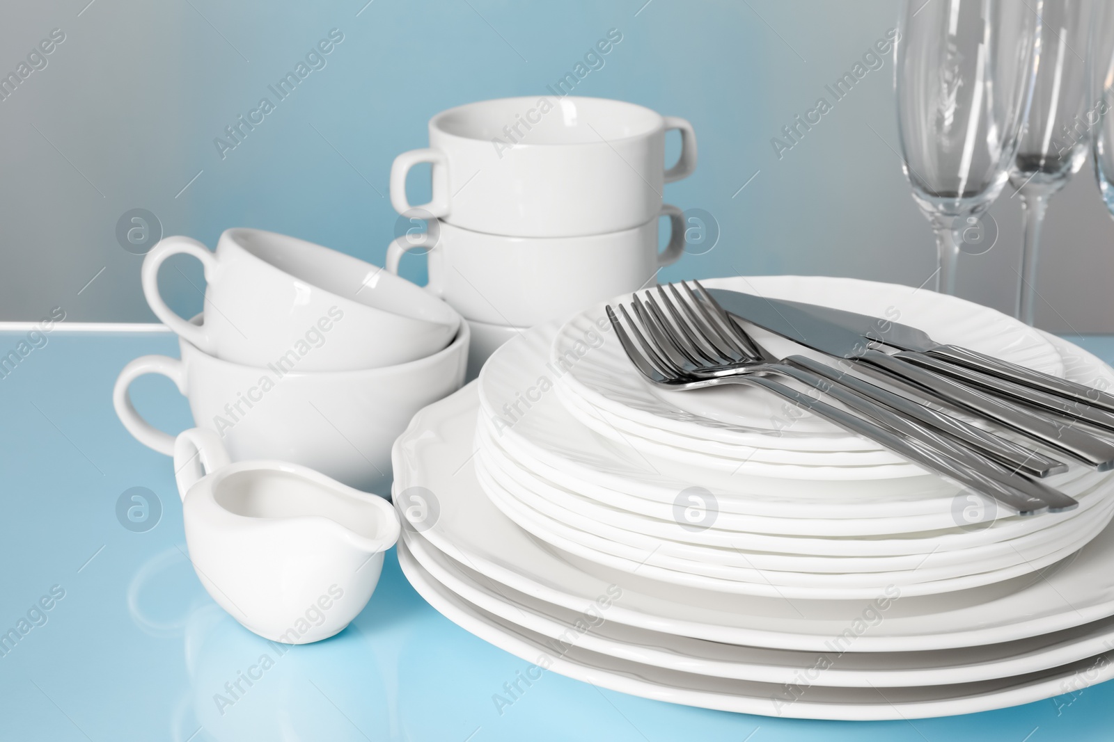 Photo of Set of clean dishes, glasses and cutlery on light blue table, closeup