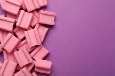 Photo of Tasty pink chewing gums on purple background, flat lay. Space for text