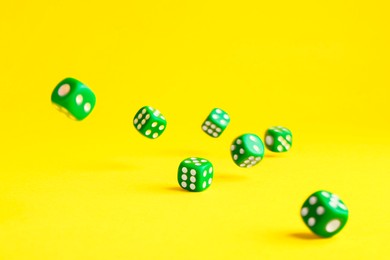Photo of Many green game dices falling on yellow background