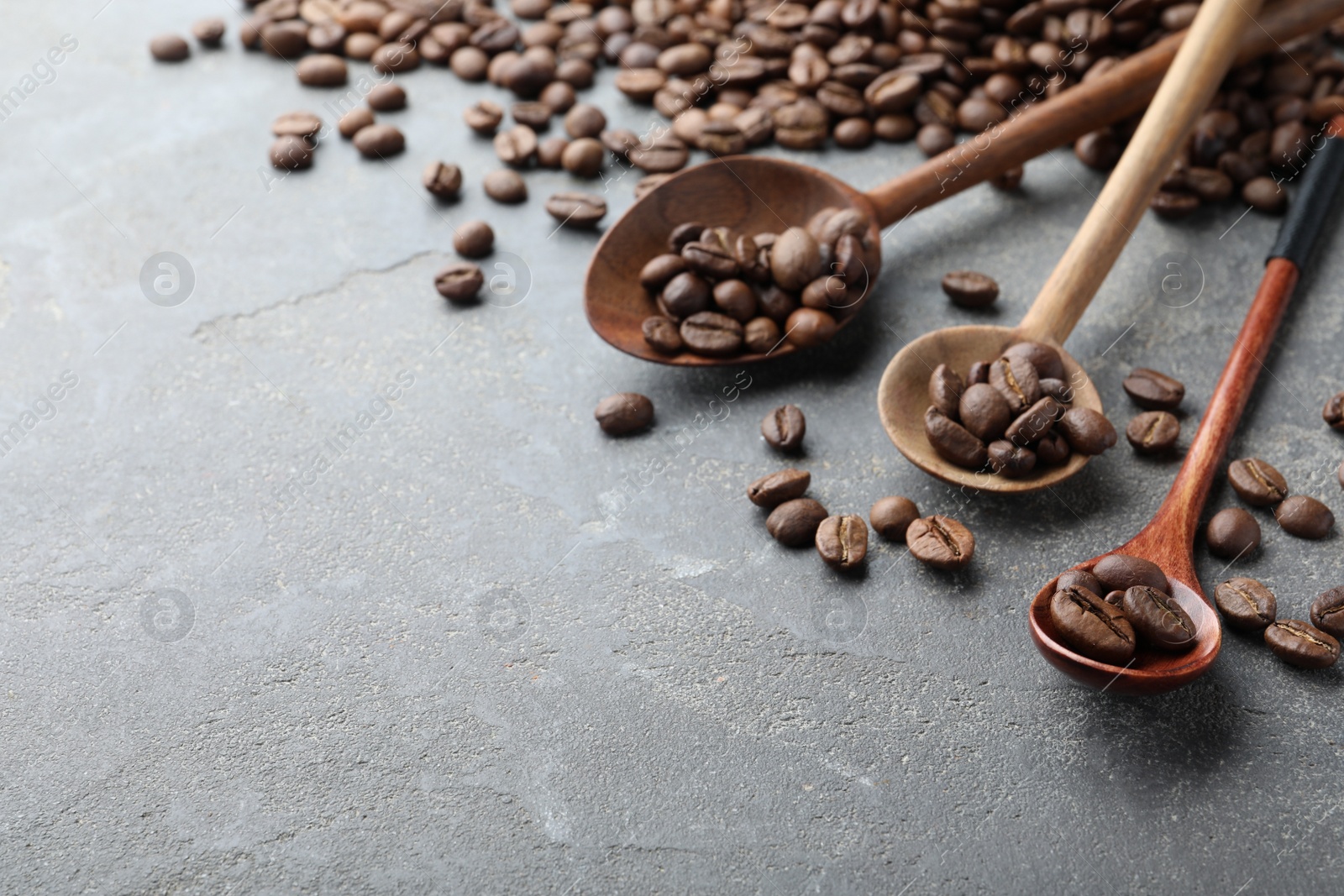 Photo of Wooden spoons with roasted coffee beans on grey table, closeup. Space for text