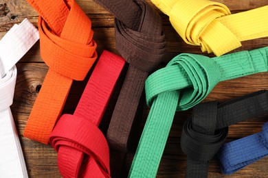 Colorful karate belts on wooden background, flat lay